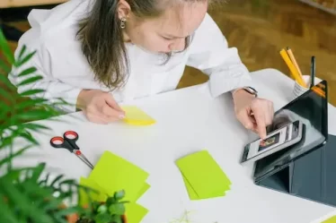 imagem de menina escrevendo em bloco de notas enquanto usa aplicativo de estudos no celular