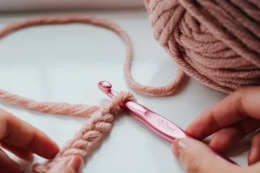 mão segurando uma agulha rosa e fios rosa de crochê
